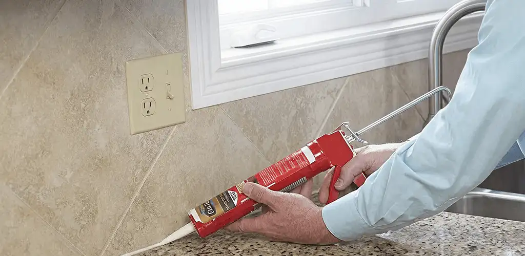 Handyman applying caulk along a kitchen backsplash and countertop seam in Cedar Rapids, IA